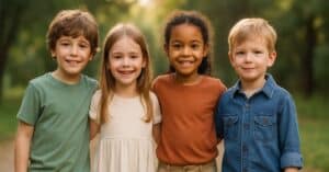 Cuatro niños sonrientes de diferentes etnias posan juntos en un parque soleado, vistiendo ropa cómoda y colorida, representando el vínculo entre ropa infantil y autoestima.